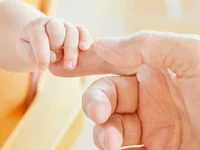 Ручка малыша держит палец